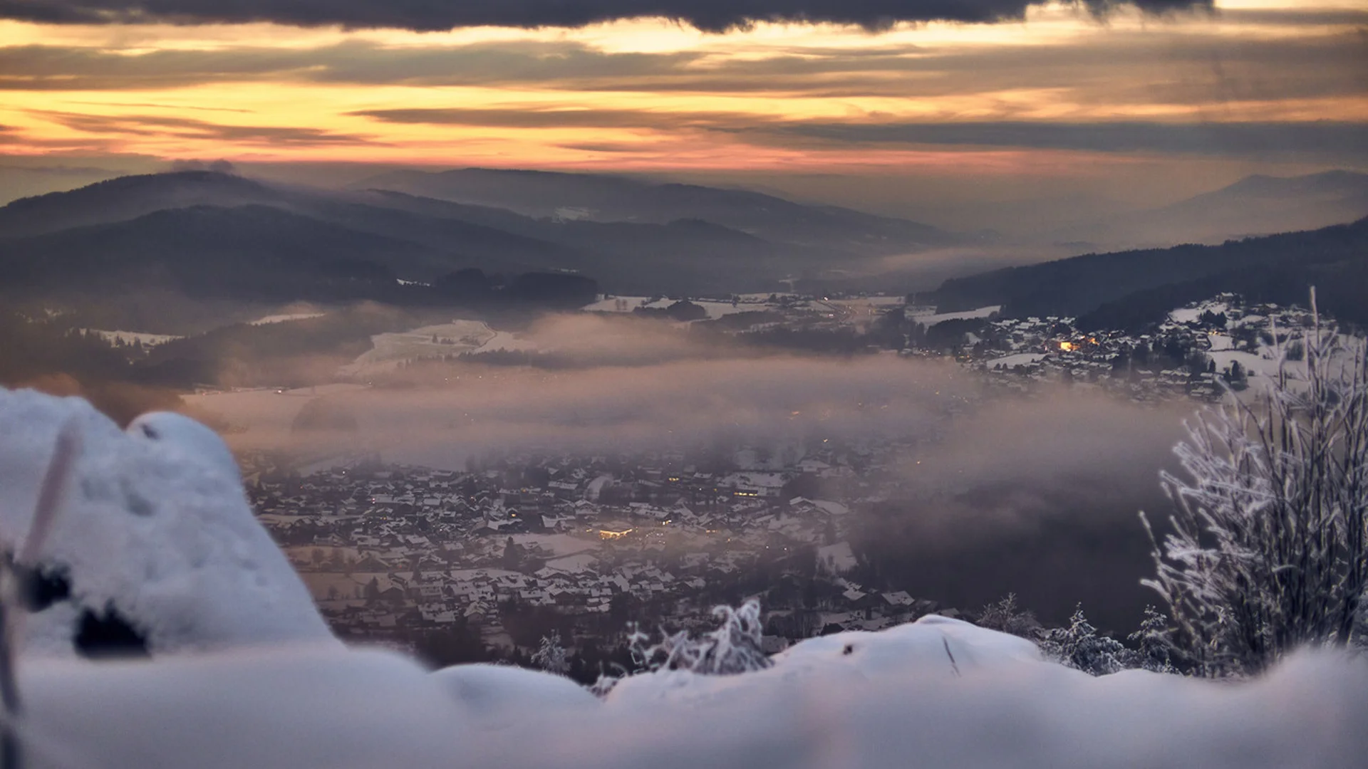 Verschneites Tal mit Nebel und Sonnenuntergang hinter Bergen