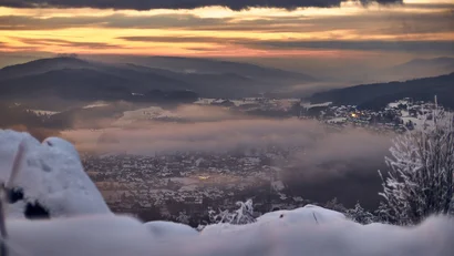Verschneites Tal mit Nebel und Sonnenuntergang hinter Bergen