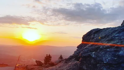 Sonnenuntergang über felsigem Berg mit Bäumen und Wolken