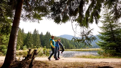 Familie spaziert neben einem See im Wald an einem bewaldeten Berg