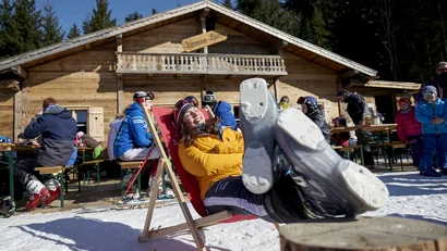 Frau in Skiausrüstung entspannt auf Liegestuhl vor Berghütte im Schnee