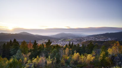 Herbstlicher Ausblick auf eine Stadt in einem bewaldeten Tal bei Sonnenuntergang