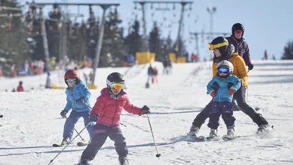 Kinder beim Skifahren auf verschneiter Piste mit Erwachsenen bei klarem Himmel