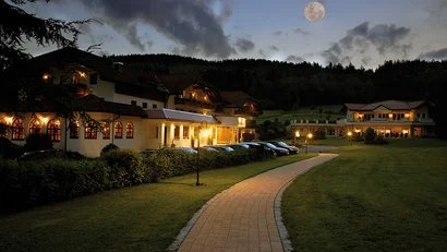 Abendaufnahme eines beleuchteten Hauses mit Vollmond und Weg im Vordergrund