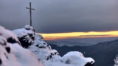 Schneebedeckter Berggipfel mit Kreuz und Sonnenuntergang