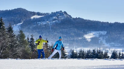 Zwei Personen beim Skilanglauf in verschneiter Winterlandschaft mit Bergen