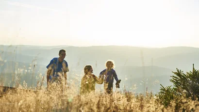 Vater mit zwei Kindern beim Wandern in sonniger Berglandschaft