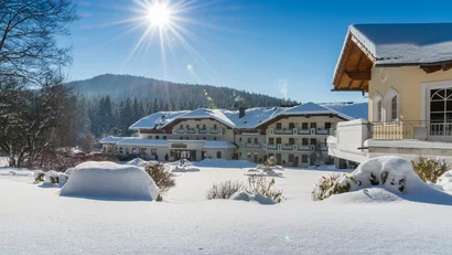 Winterliche Landschaft mit schneebedecktem Hotelgebäude unter sonnigem blauem Himmel
