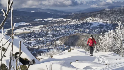 Frau wandert mit Stöcken durch verschneite Berge mit Blick auf Stadt im Tal