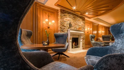 Gemütliche Lounge mit Kamin, runden Holztischen und grauen Sesseln