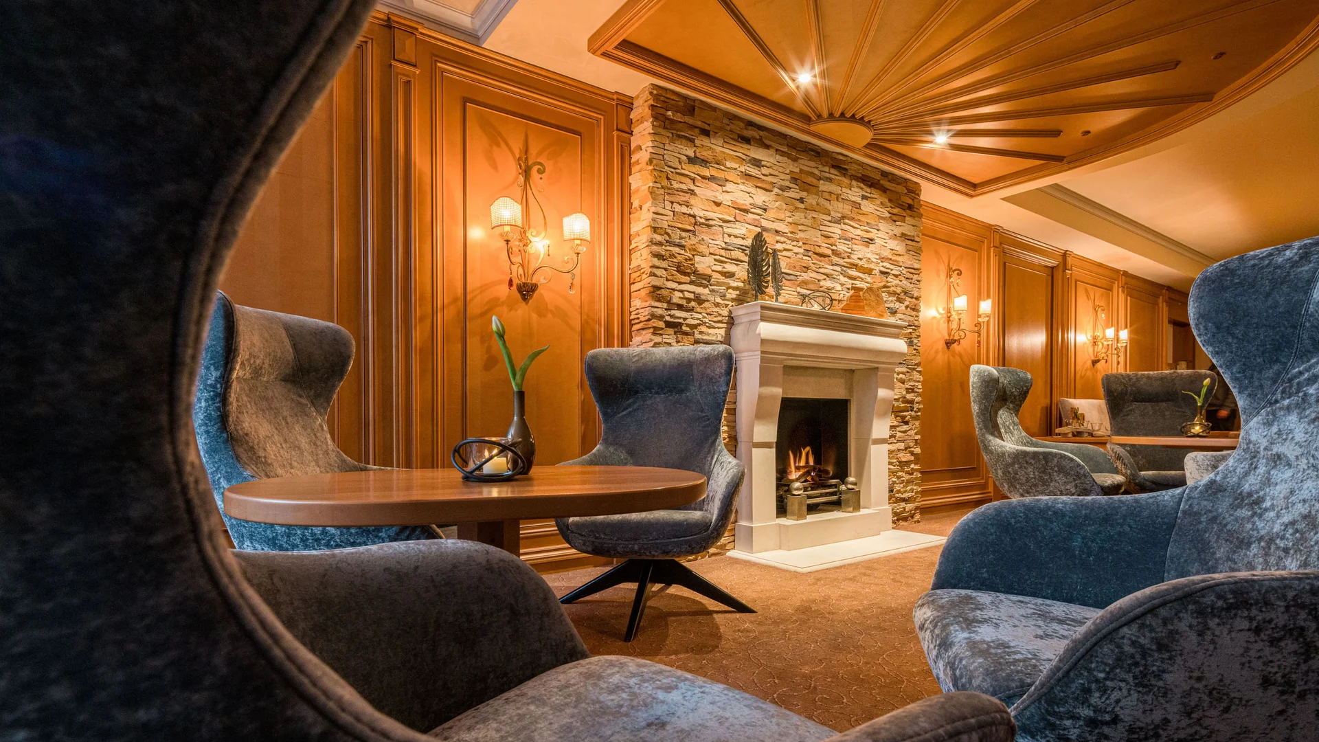 Gemütliche Lounge mit Kamin, runden Holztischen und grauen Sesseln
