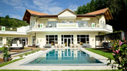 Haus mit Pool und Terrasse vor bewaldetem Hügel bei klarem Himmel