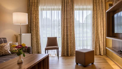 Gemütliches Wohnzimmer mit Stuhl, Hocker, Sofa und großen Fenster mit Gardinen