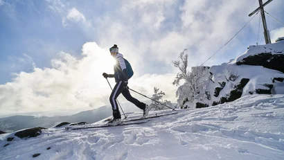 Skifahrer bei Sonnenaufgang auf verschneiter Bergspitze mit Kreuz