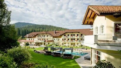 Hotel mit Garten, Pool und Liegen vor bewaldetem Berg