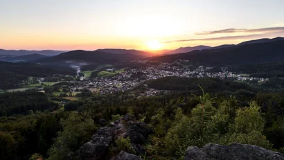 Blick auf ein Tal mit Dorf bei Sonnenuntergang in bergiger Landschaft
