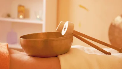 Klangschale und Schlägel auf einem Massagetisch mit warmem Licht