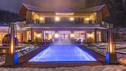 Beleuchteter Außenpool vor einem Hotel bei Nacht im Schnee