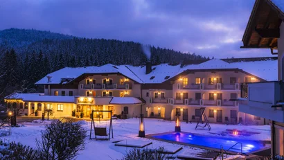 Hotel im verschneiten Winter mit beleuchtetem Außenpool und Tannenwald im Hintergrund