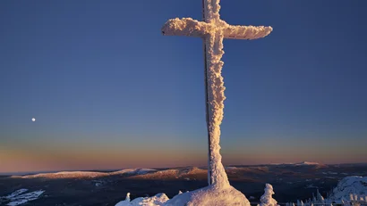 Vereistes Kreuz auf einem Berggipfel bei Sonnenaufgang