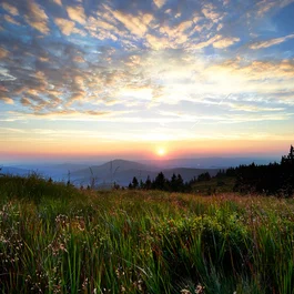 Sonnenuntergang über grüner Bergwiese mit bewölktem Himmel