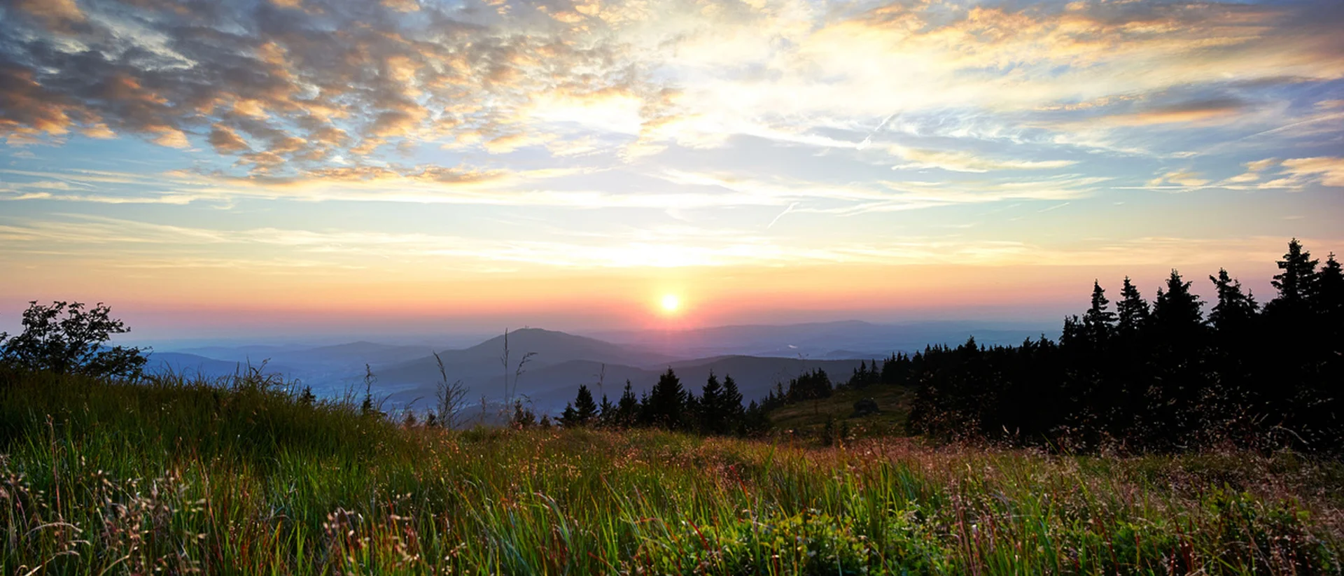 Sonnenuntergang über grüner Bergwiese mit bewölktem Himmel