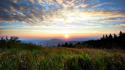 Sonnenuntergang über grüner Bergwiese mit bewölktem Himmel